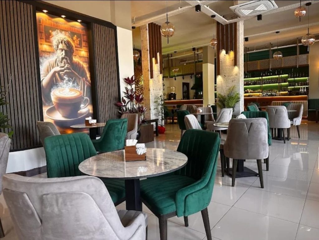 Halibas Art Cafe & Gallery iç salonu, yeşil sandalyeler ve kahve temalı duvar resmi